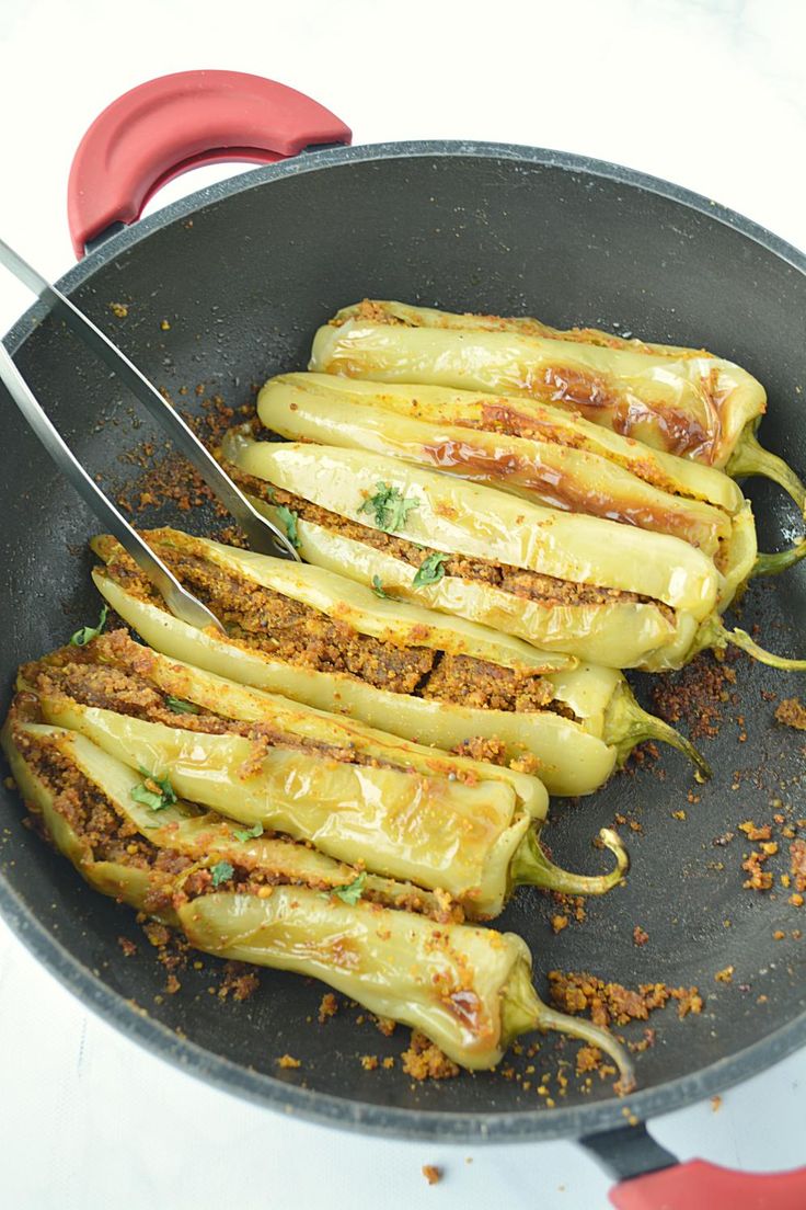 some food is being cooked in a frying pan with tongs on the side