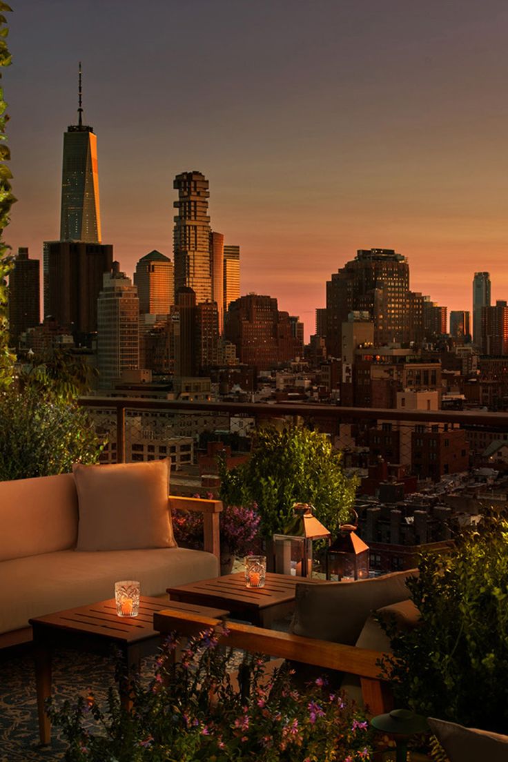 an outdoor seating area overlooking the city at sunset with candles lit on it and greenery in foreground