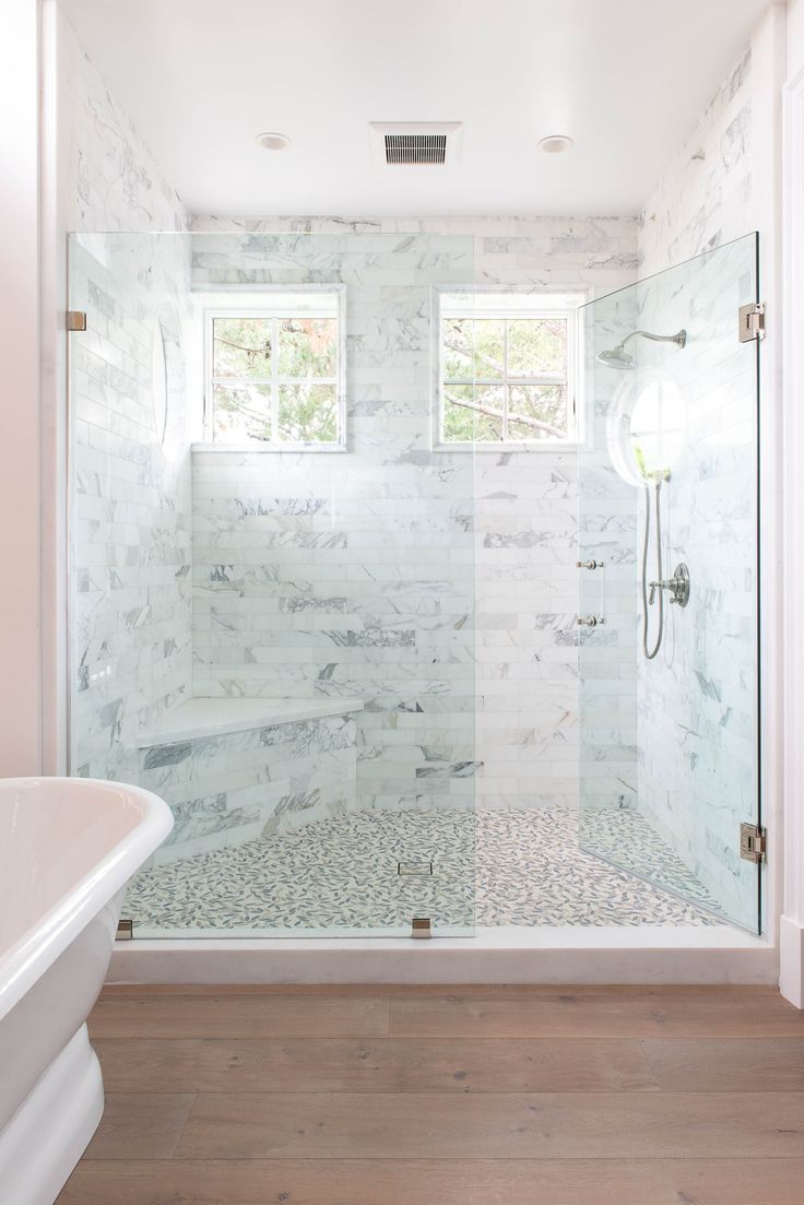 a bathroom with a walk in shower next to a white tub and wooden flooring