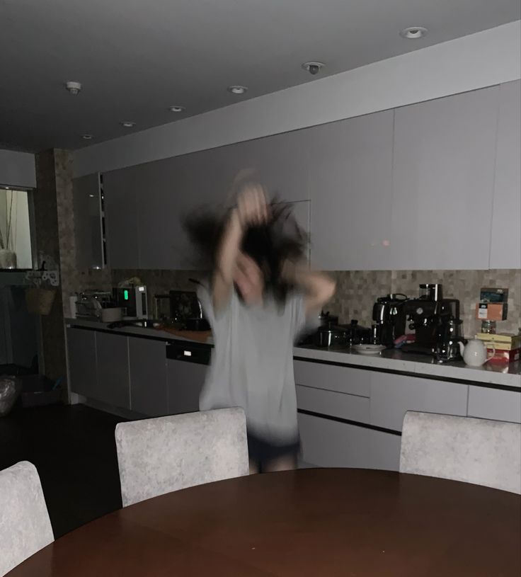 a woman is dancing in the kitchen with her hair blowing back into the air and she's wearing a gray shirt