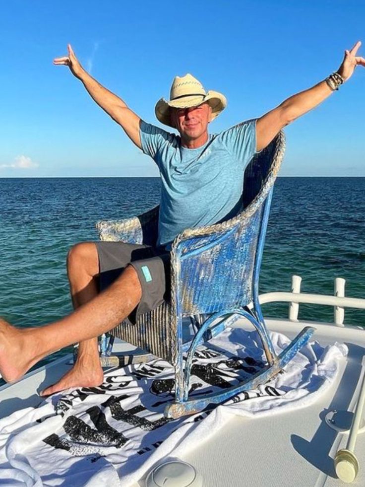 a man sitting in a chair on top of a boat with his arms outstretched up