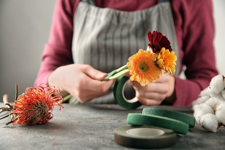 a woman is holding flowers and scissors on a table next to some cotton balls, garlic and other things