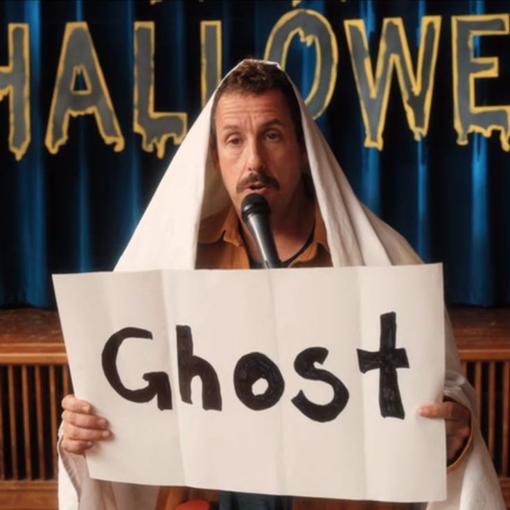 a man holding a sign with the word ghost written on it while standing in front of a microphone