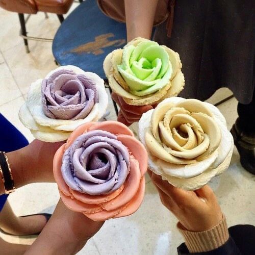 four different colored cupcakes being held up in the air by people's hands