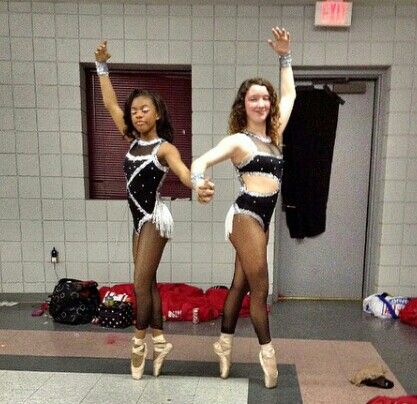 two young women in black and white outfits dancing on the floor with their hands up