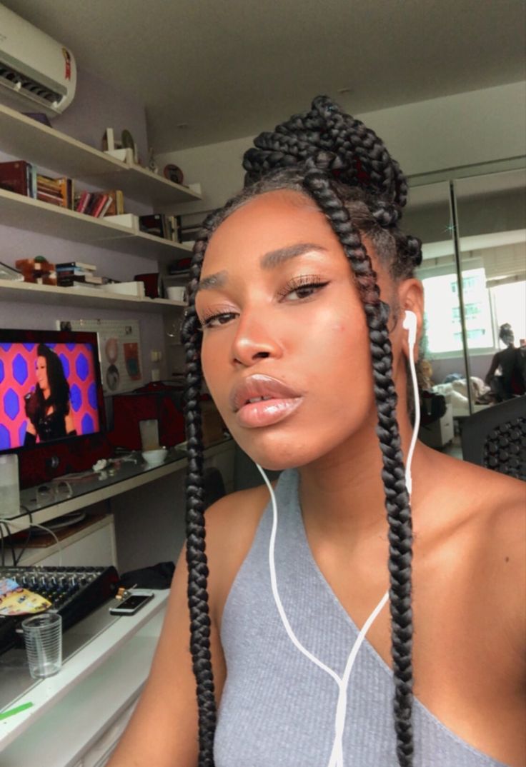 a woman with long braids sitting in front of a computer desk and listening to headphones