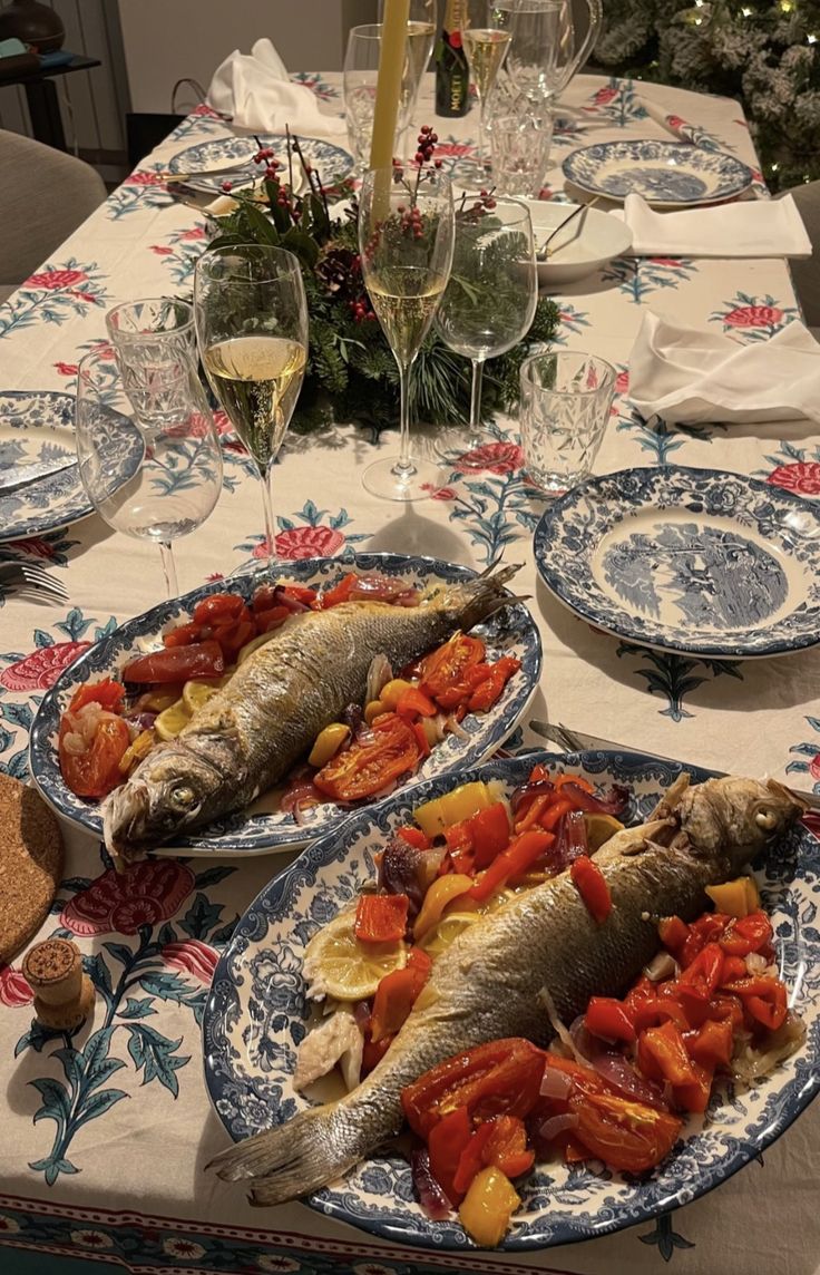 two plates with fish and vegetables on them sitting on a table next to wine glasses