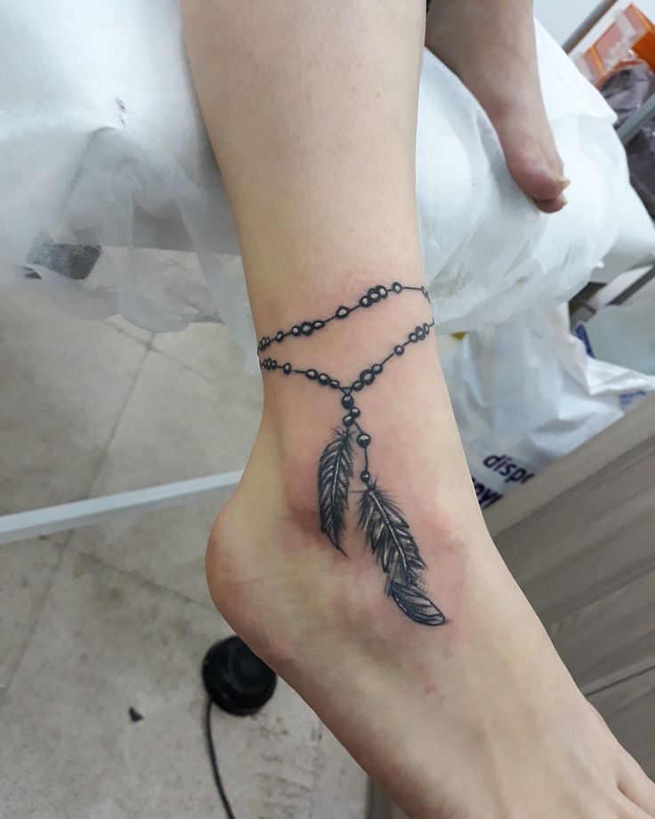 a woman's foot with a chain and an arrow tattoo on her left ankle