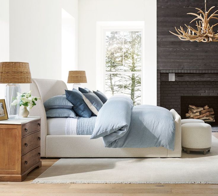 a bed with blue sheets and pillows in front of a fireplace