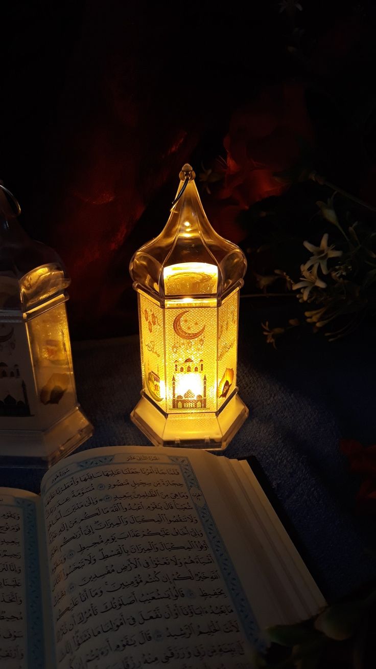 an open book sitting on top of a table next to a lit lantern