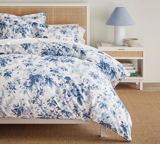 a bed with blue and white comforters in a bedroom next to a lamp on a table