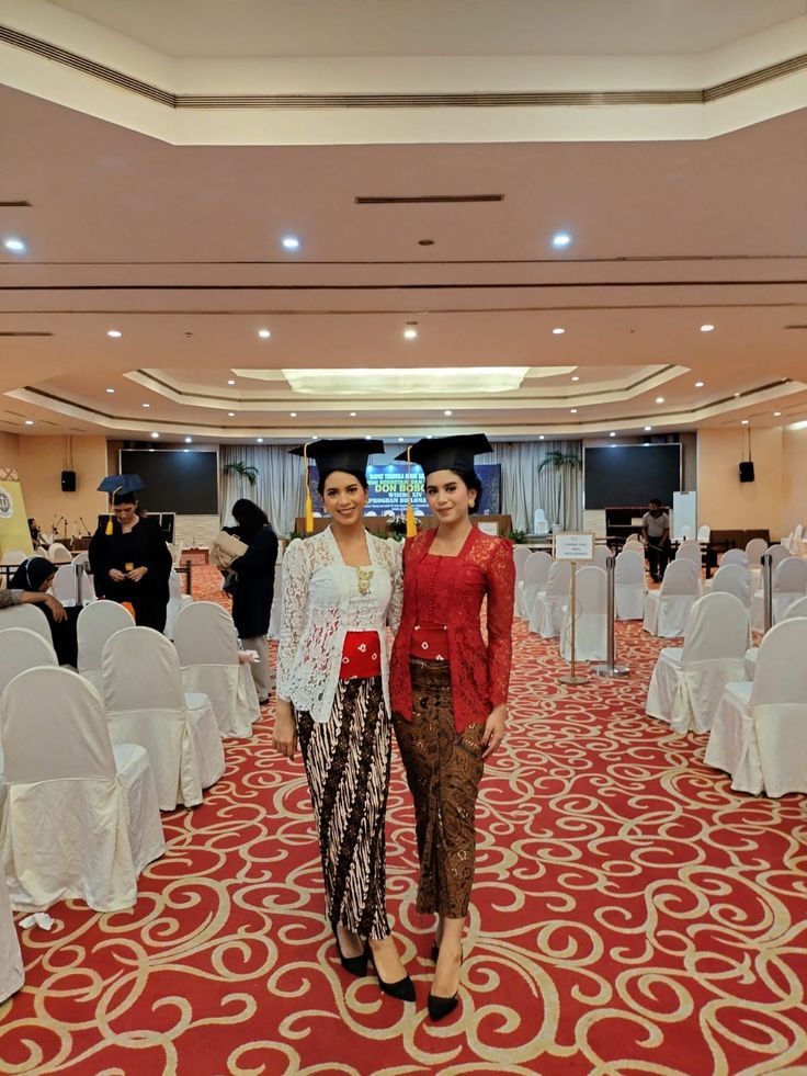 two women standing next to each other in a banquet hall with white tables and chairs