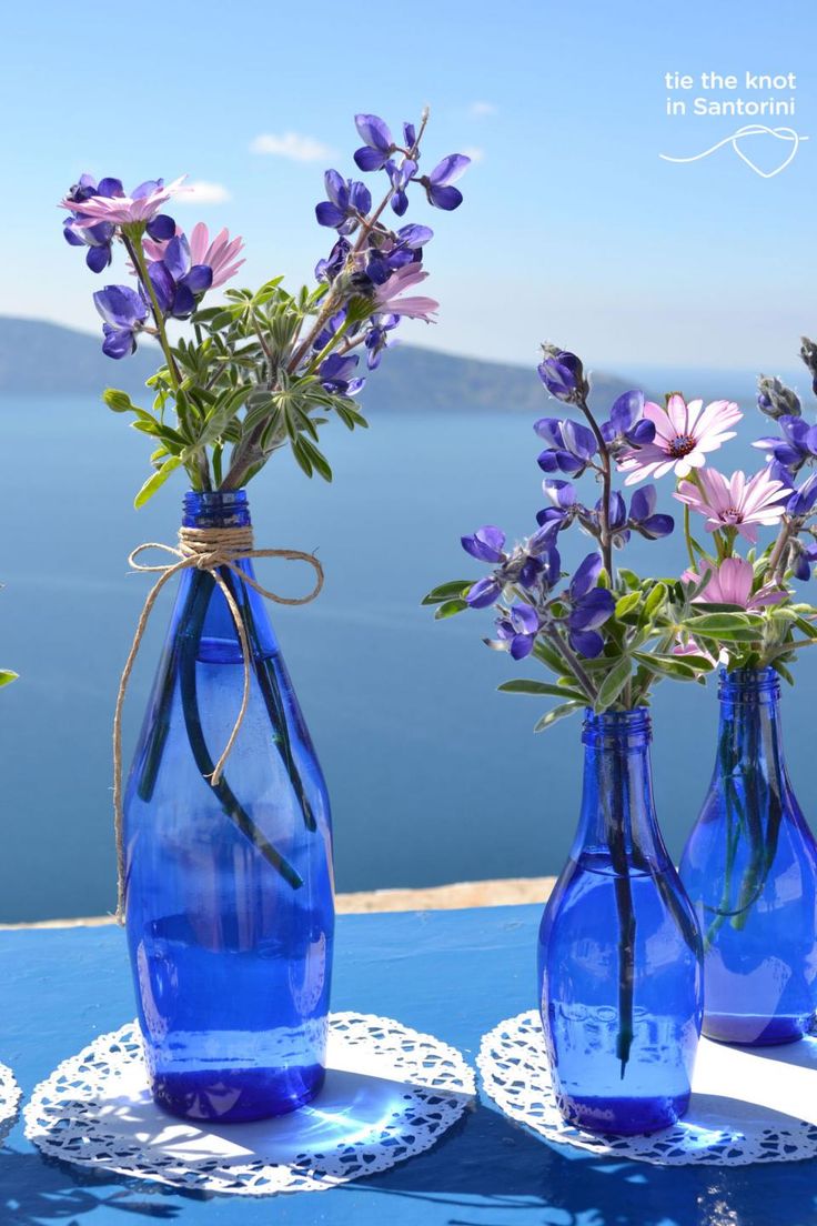 two blue vases with flowers in them sitting on a table next to the ocean