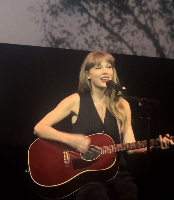 a woman holding a guitar and singing into a microphone