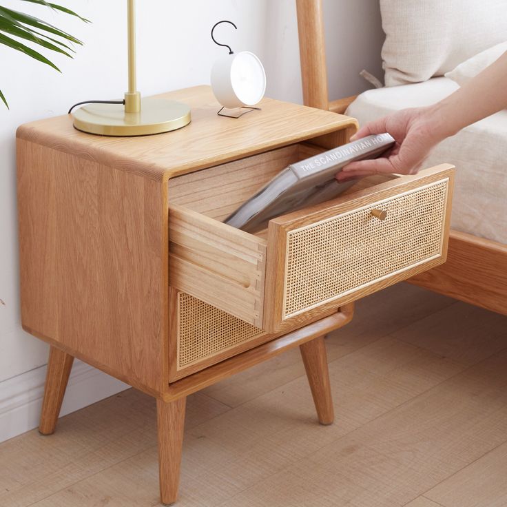 a person holding a remote control in their hand near a bed with a wooden night stand