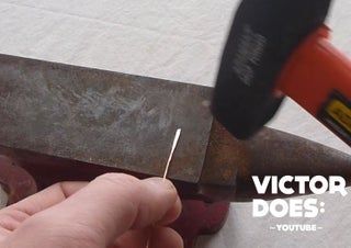 a hand holding a pair of scissors over a piece of metal with the words victory does on it