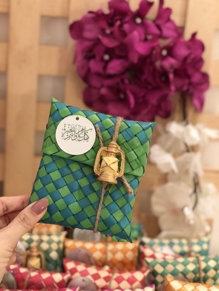 a person holding up a small green and blue gift bag with a bell on it