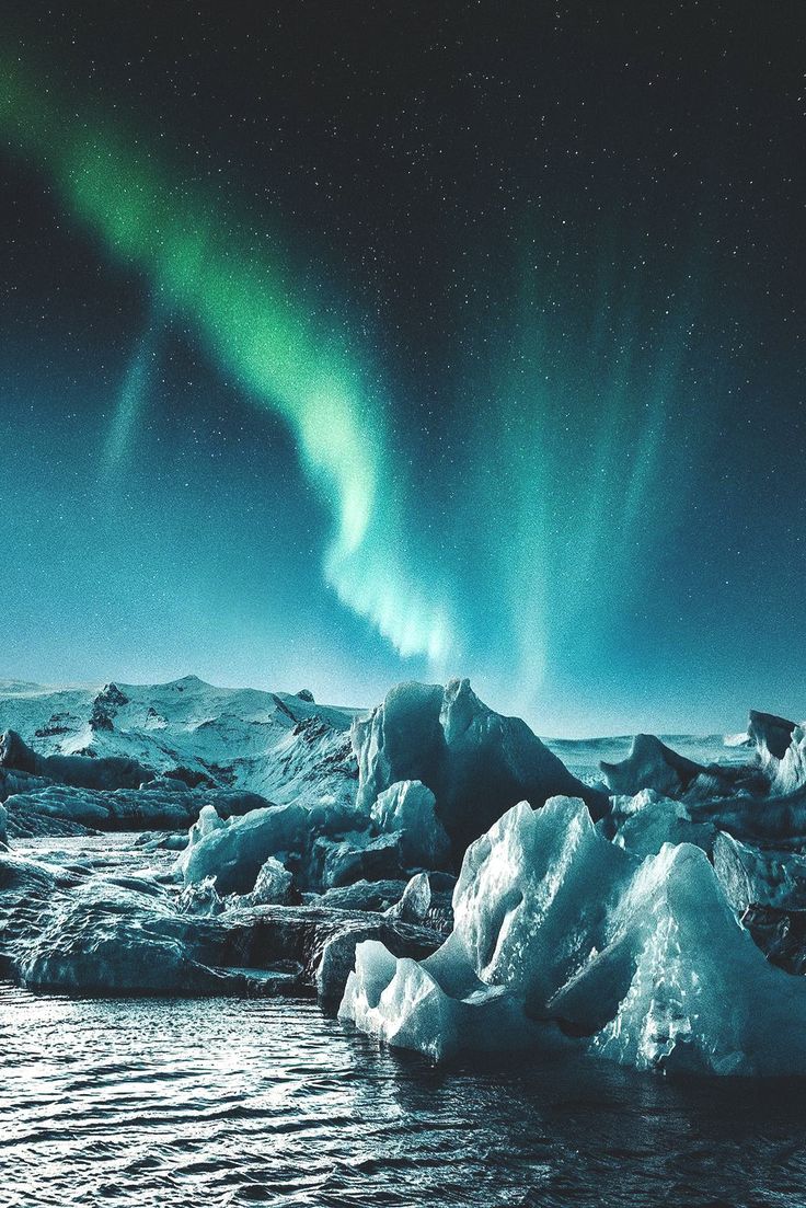 an aurora bore is seen above icebergs in the arctic waters, with bright green lights