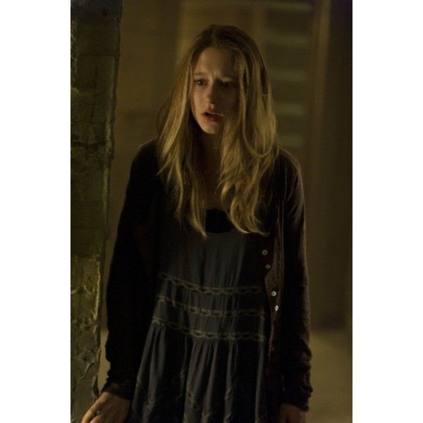 a woman standing next to a brick wall in a dark room with the light on