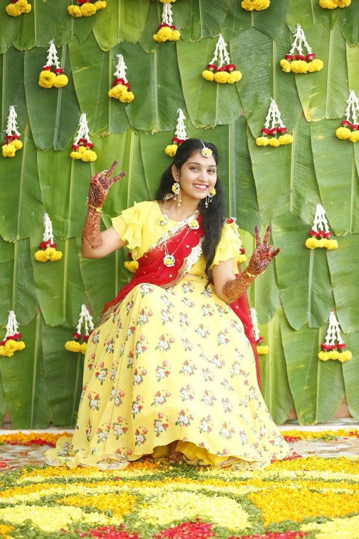 a woman in a yellow and red dress sitting on a flowered floor with her hands up