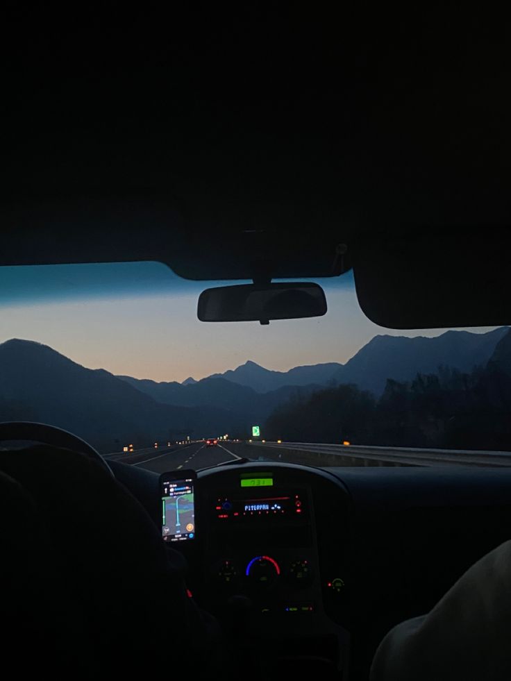 the view from inside a car driving down a highway at night with mountains in the distance