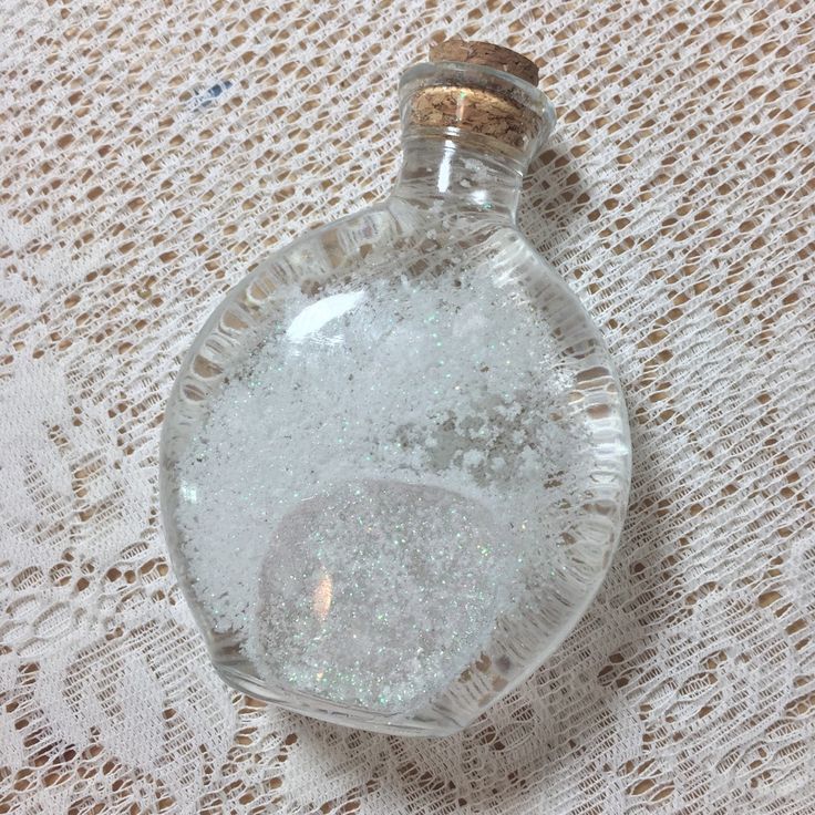 a glass bottle filled with water sitting on top of a lace covered tablecloth next to a wooden stopper