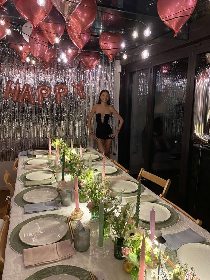 a woman standing in front of a table set for a party with pink and silver balloons