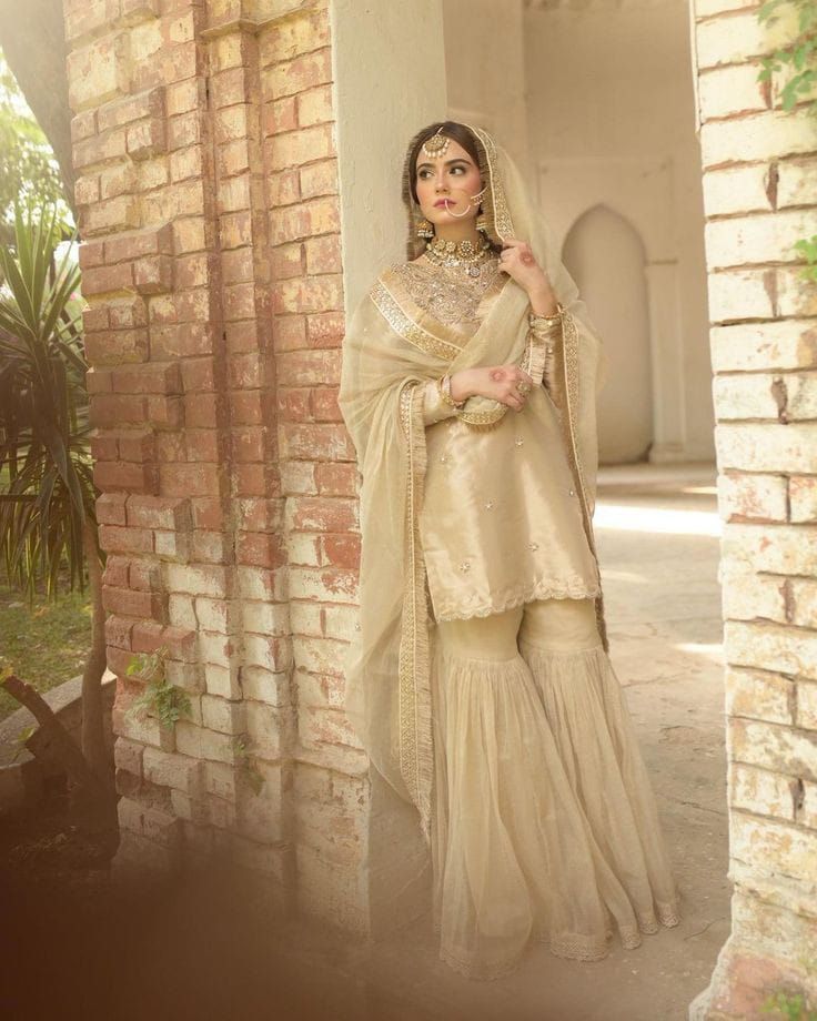 a woman wearing a beige outfit standing in front of a brick wall