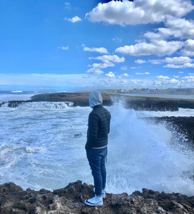 a person standing on top of a rocky cliff next to the ocean and crashing waves