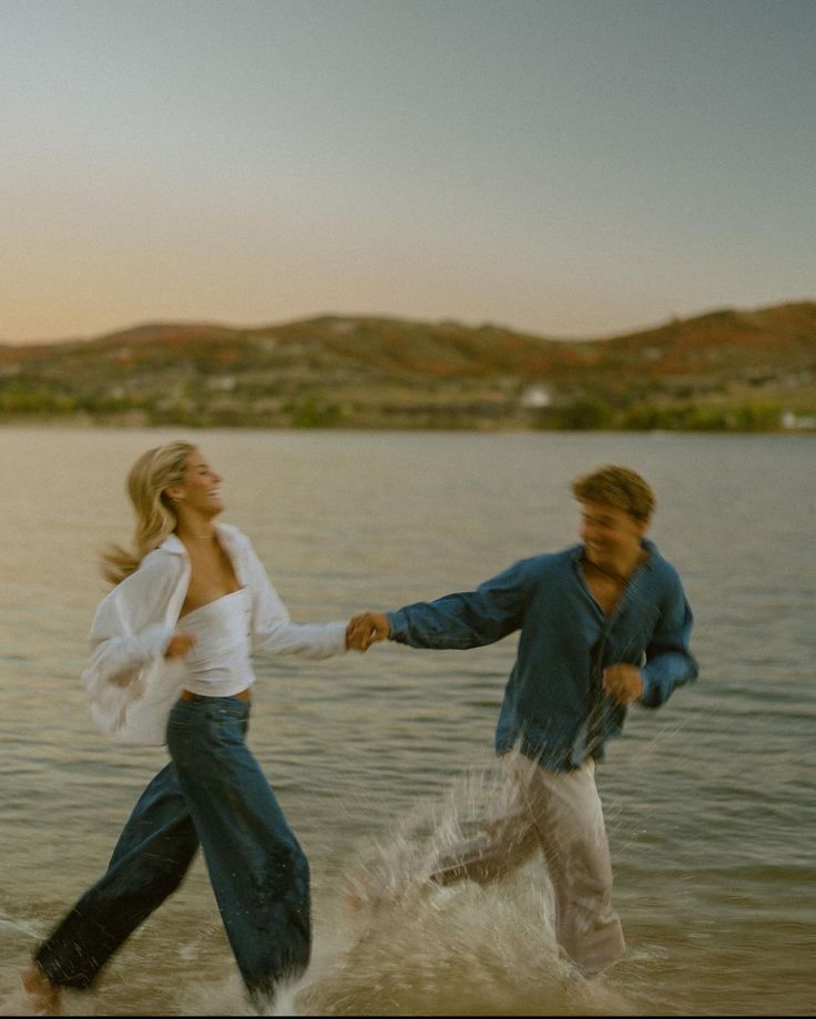 two people are running in the water holding hands and smiling as they run towards each other