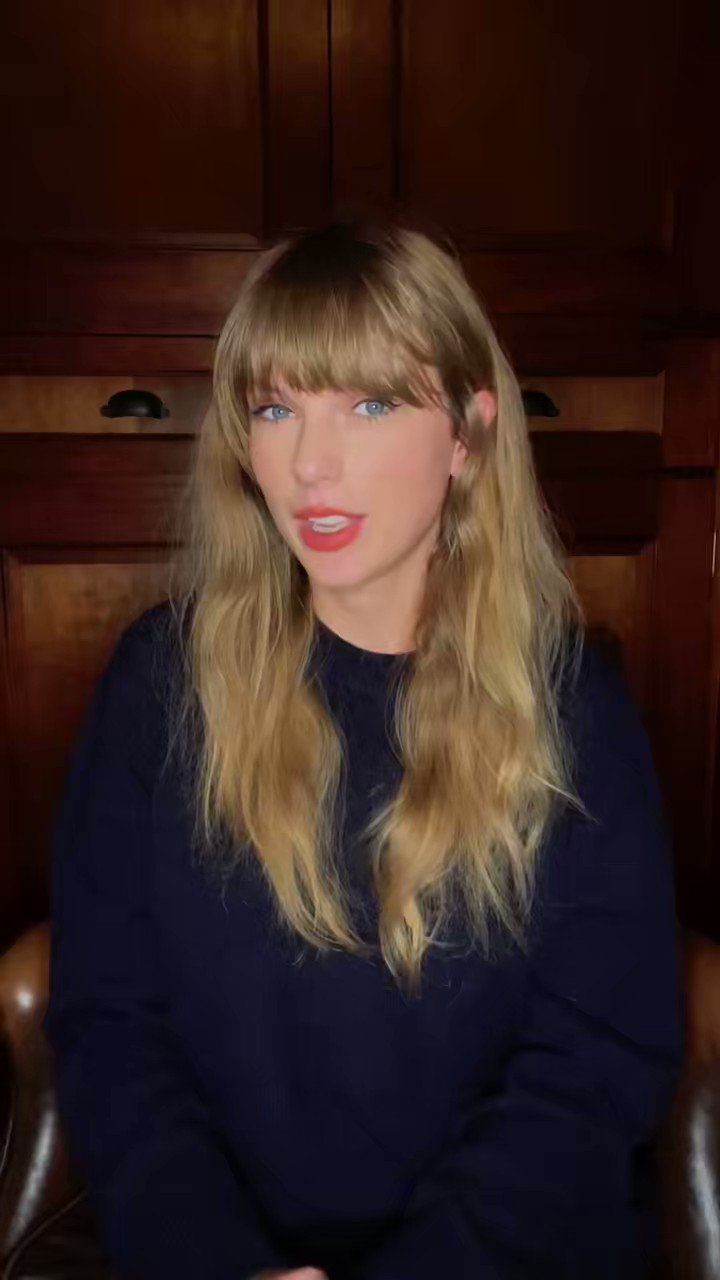 a woman with long blonde hair and blue eyes sitting in a chair wearing a black sweater