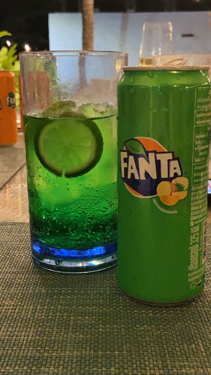 a can of soda and a glass with a lime slice on the rim sitting on a table