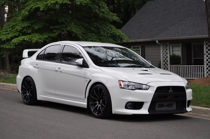 a white car is parked on the side of the road in front of a house