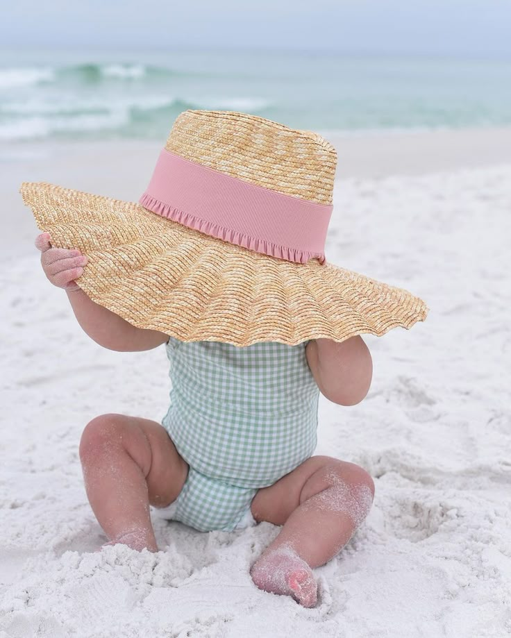 a baby sitting in the sand wearing a straw hat