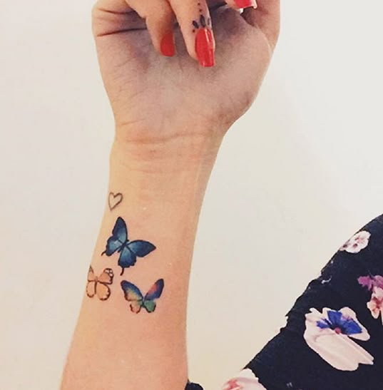 a woman's arm with butterflies on it and a red manicured nail polish