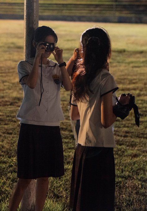 two girls standing next to each other near a tree and one is looking through a pair of binoculars