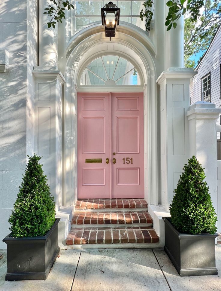 a pink front door with two planters on either side and an arch above it