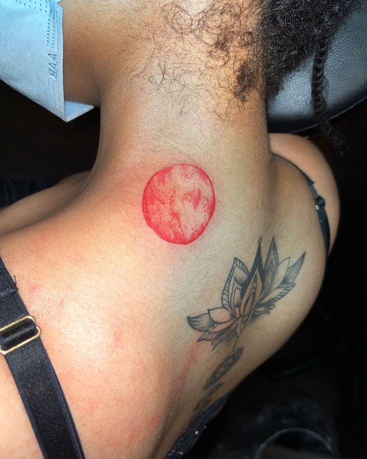 a woman's back with a tattoo on her left side and a red circle in the middle