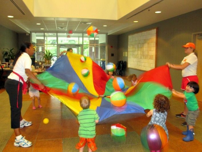 children playing with colorful kites and balls in an office building lobby while adults watch