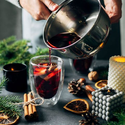 a person pours red wine into a glass with cinnamon sticks and pine cones around it