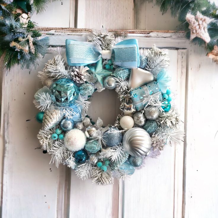 a christmas wreath with blue and silver ornaments hanging on a white wooden door next to pine cones