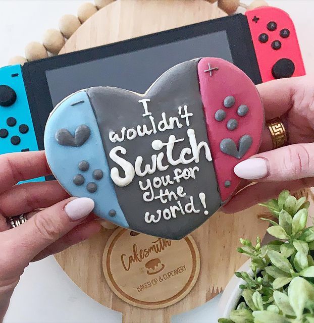 a woman holding up a heart shaped cookie in front of a video game controller with the words i wouldn't switch your time for this world on it