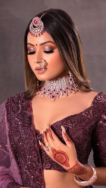 a woman in a purple outfit with jewelry on her head and hands around her chest