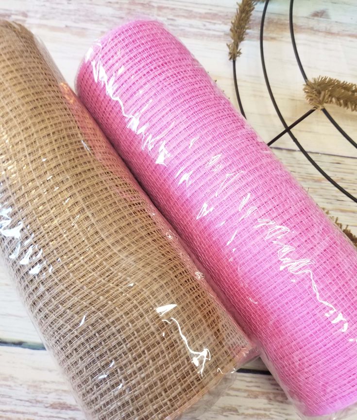 two rolls of pink yoga mat sitting next to each other on a wooden table with dried plants