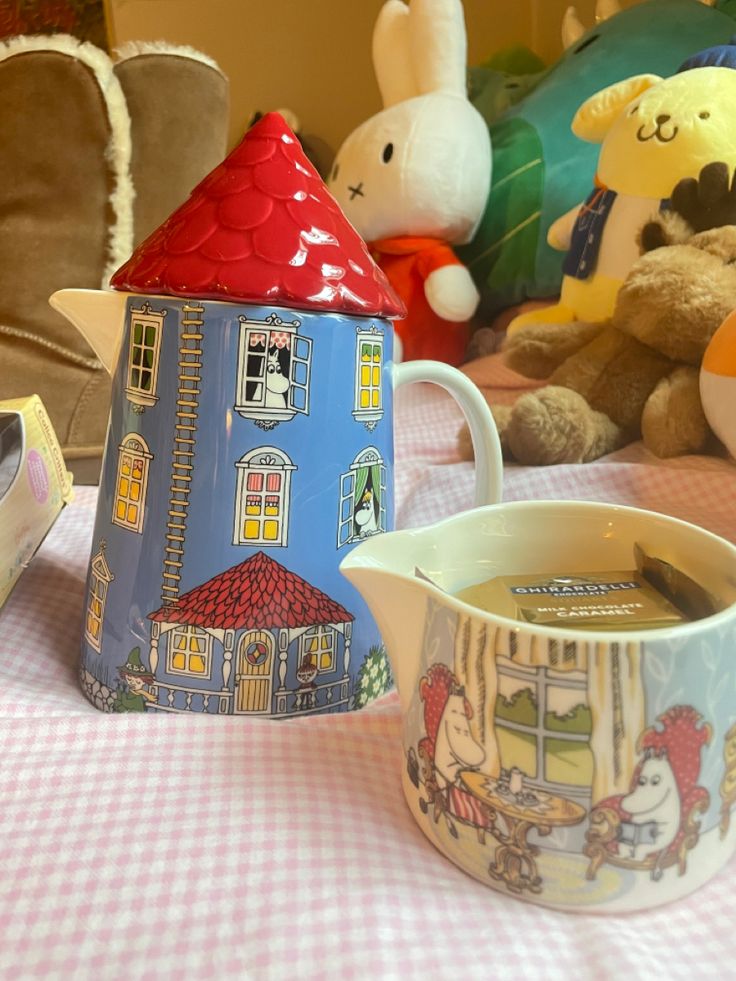 there is a tea pot with a house on it next to a cup and saucer