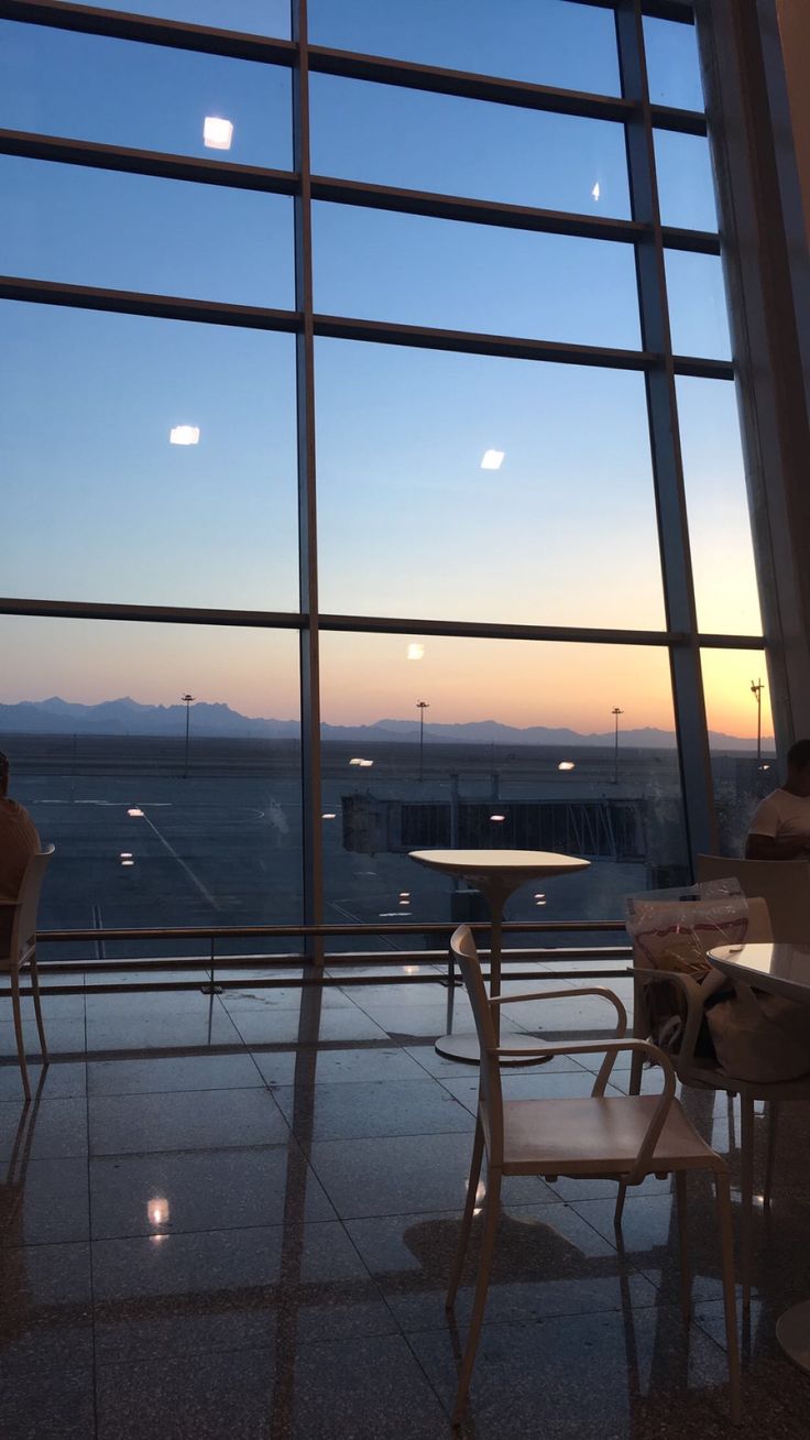 two people sitting at tables in front of large windows