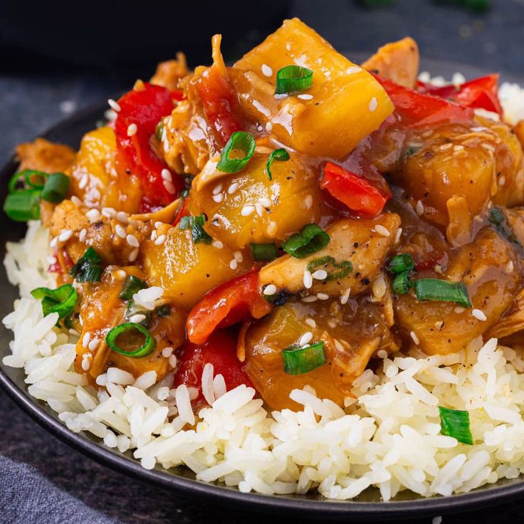 a black plate topped with rice and meat covered in sauce, garnished with green onions