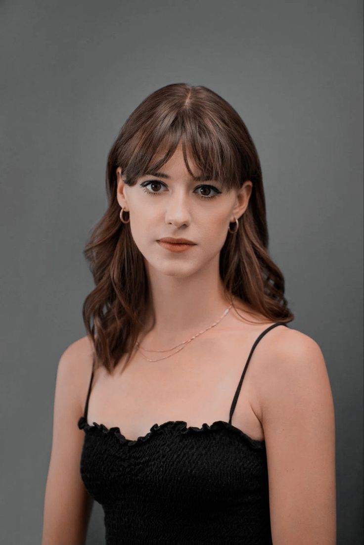 a woman with long hair wearing a black top and gold necklace, looking at the camera