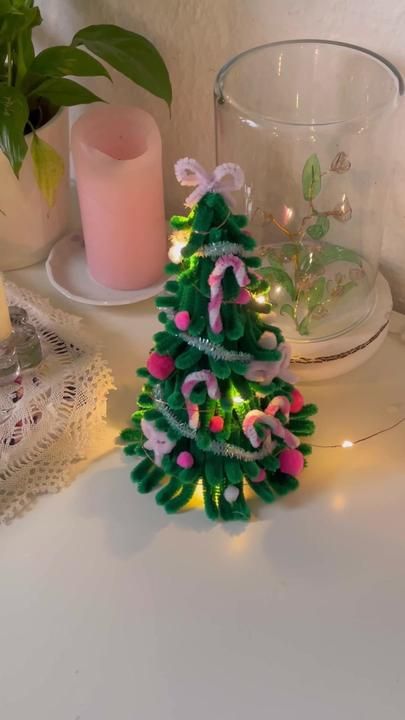 a small green christmas tree sitting on top of a table next to a lit candle