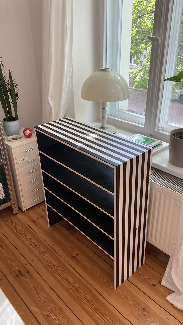 a black and white striped chest of drawers next to a window with a lamp on top